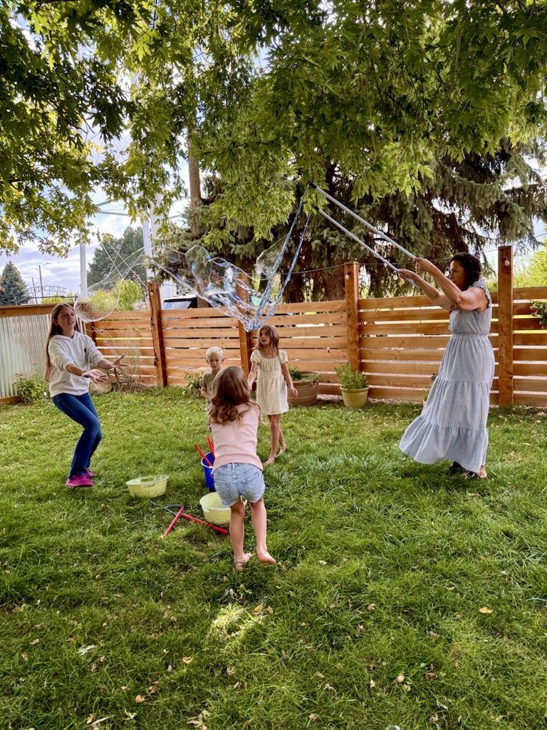 Children chasing bubbles as Jen performs in a backyard