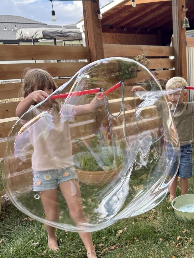 Two children making enormous bubbles with red wands